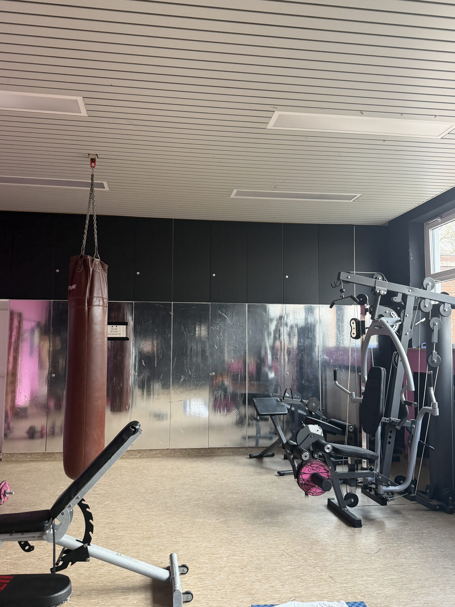 Raum mit großem Spiegel, einem Boxsack und einem Fitnessgerät zum Trainieren.