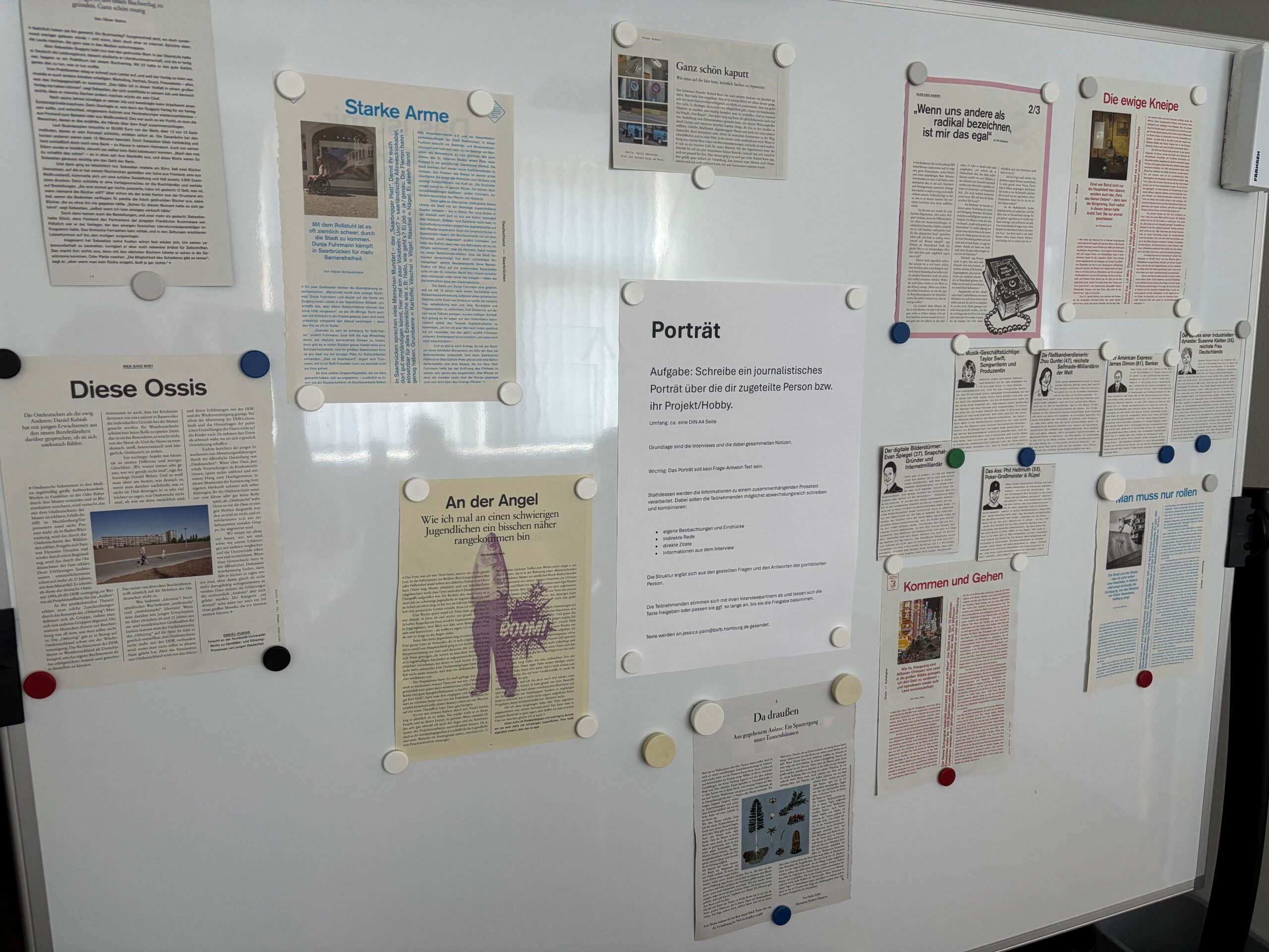 Weiße Pinnwand mit verschiedenen Zeitungsartikeln und einem Arbeitsauftrag zum journalistischen Porträt. Die Beiträge sind mit bunten Magneten befestigt.